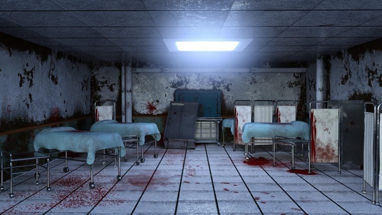Chambre d&rsquo;h&ocirc;pital abandonn&eacute;e avec plusieurs lits m&eacute;talliques vides, murs d&eacute;cr&eacute;pis et lumi&egrave;re froide entrant par les fen&ecirc;tres lat&eacute;rales.
